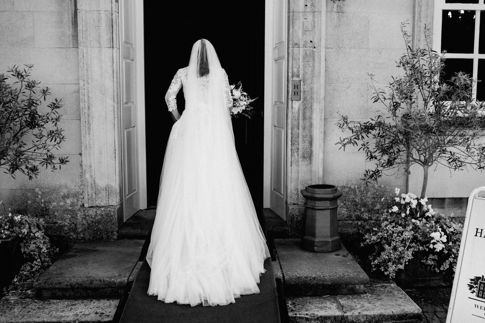 Silhouette of bride in flowing wedding dress standing in doorway of historic building.