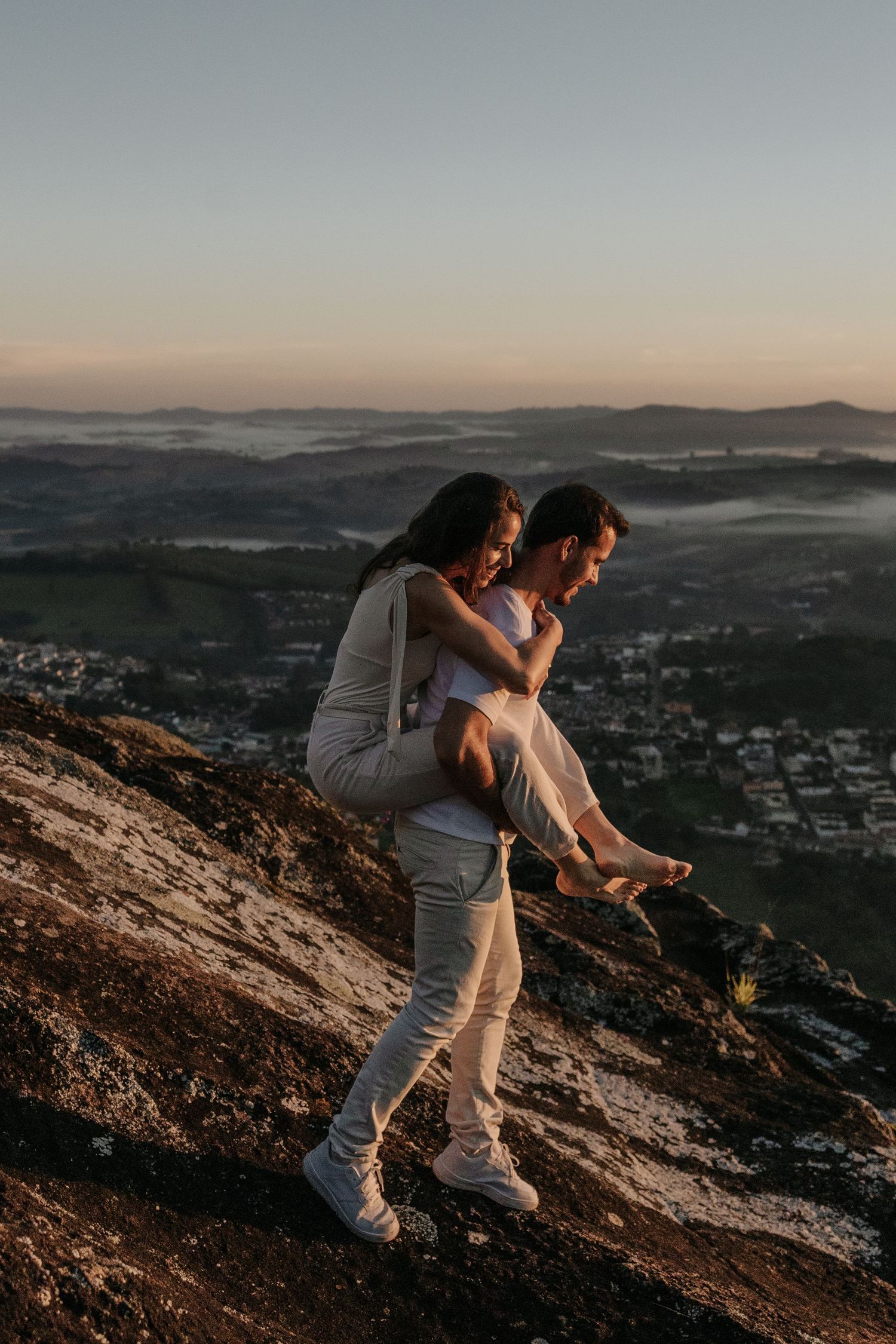 man carrying his fiance while get down of the hill with a view of ther city from the top
