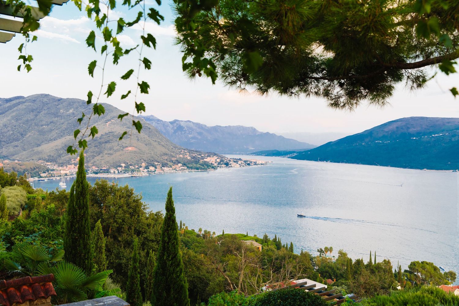 Scenic Mediterranean coastal landscape with cypress trees overlooking a tranquil bay and distant mountains.