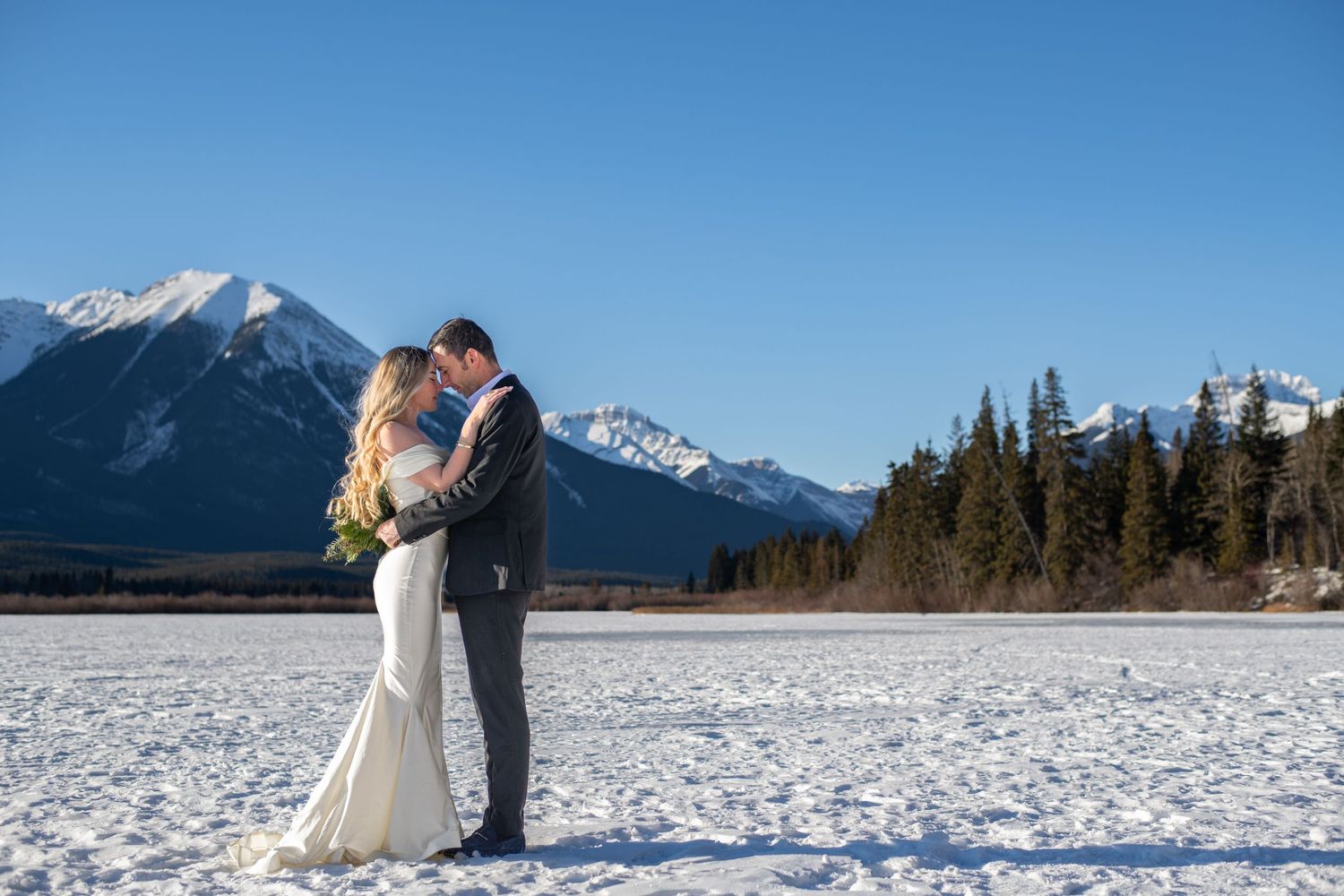 Scenic winter wedding photoshoot with snow-covered landscape and mountain backdrop.