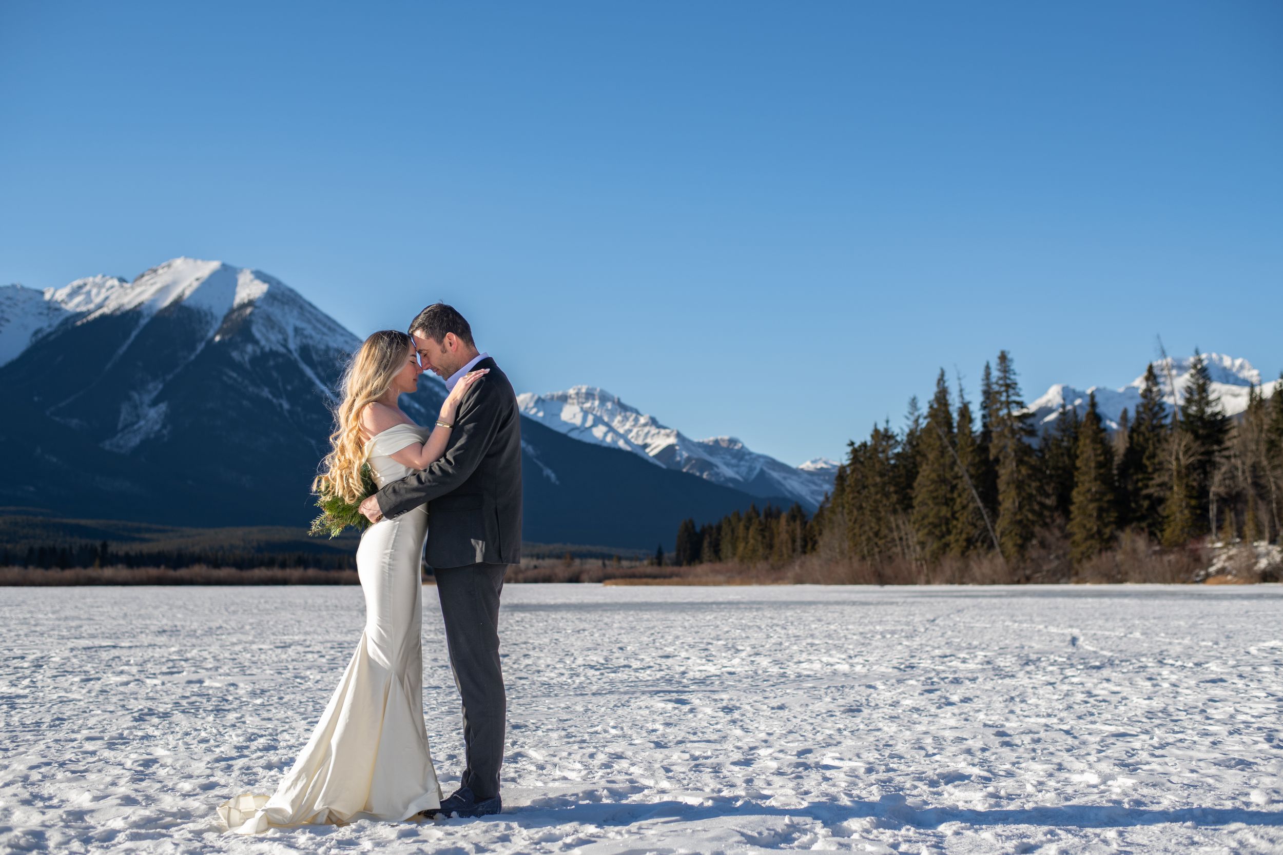 Scenic winter wedding photoshoot with snow-covered landscape and mountain backdrop.