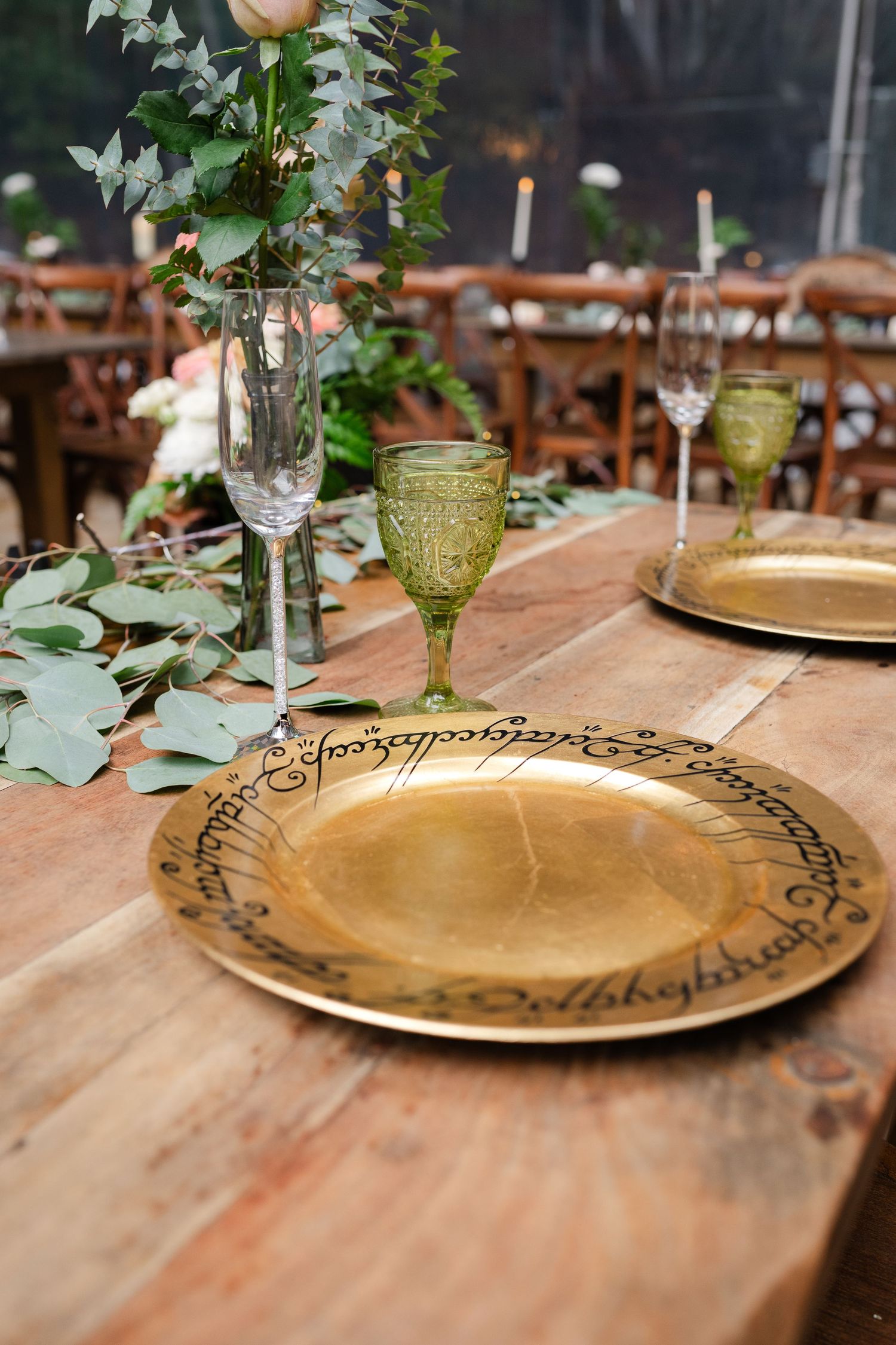 Wedding seating chart displayed on an elegant gold-framed board in a clear tent reception venue with crossback chairs.