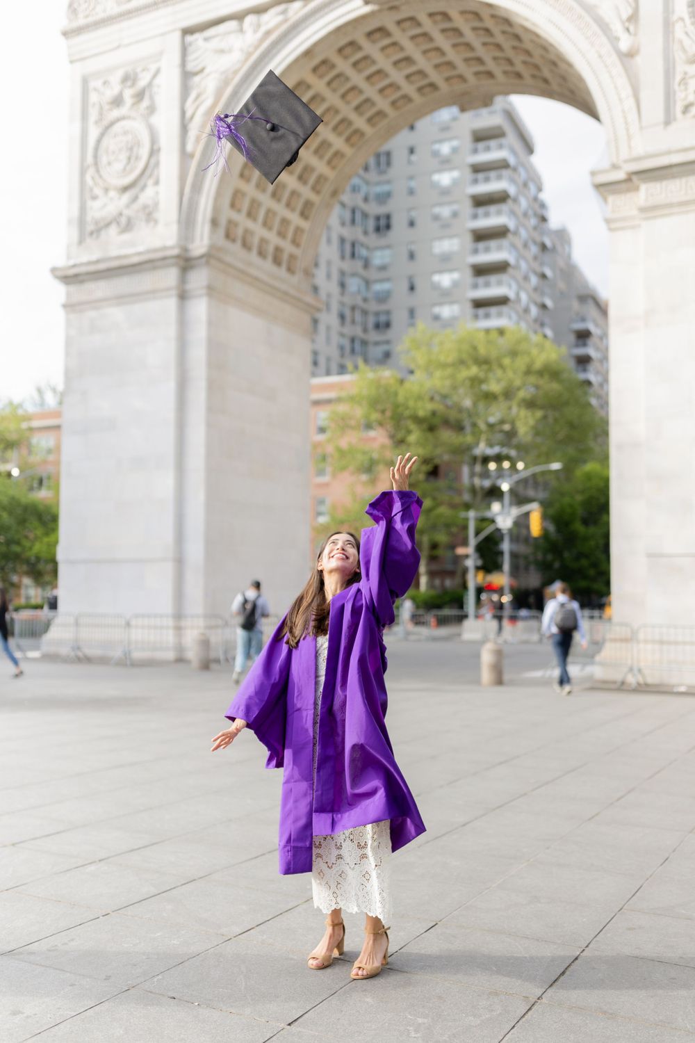 Graduate in purple robe joyfully throws cap in front of Washington Square Arch.