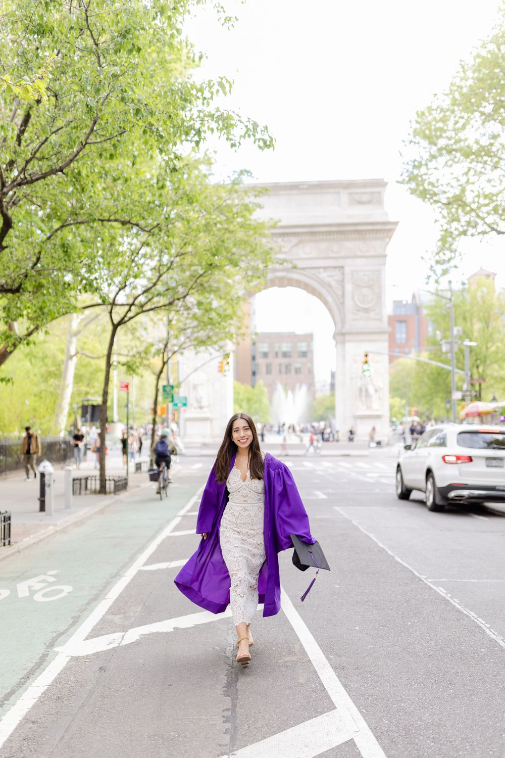 Graduate in purple regalia poses in front of Washington Square Arch in NYC.