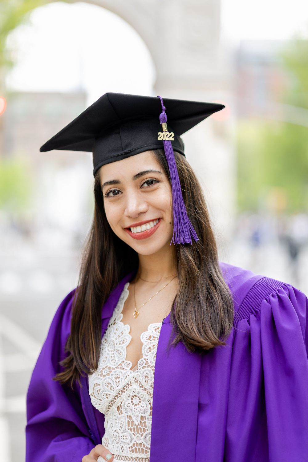 Graduate wearing purple gown and black cap with tassel smiles at camera.