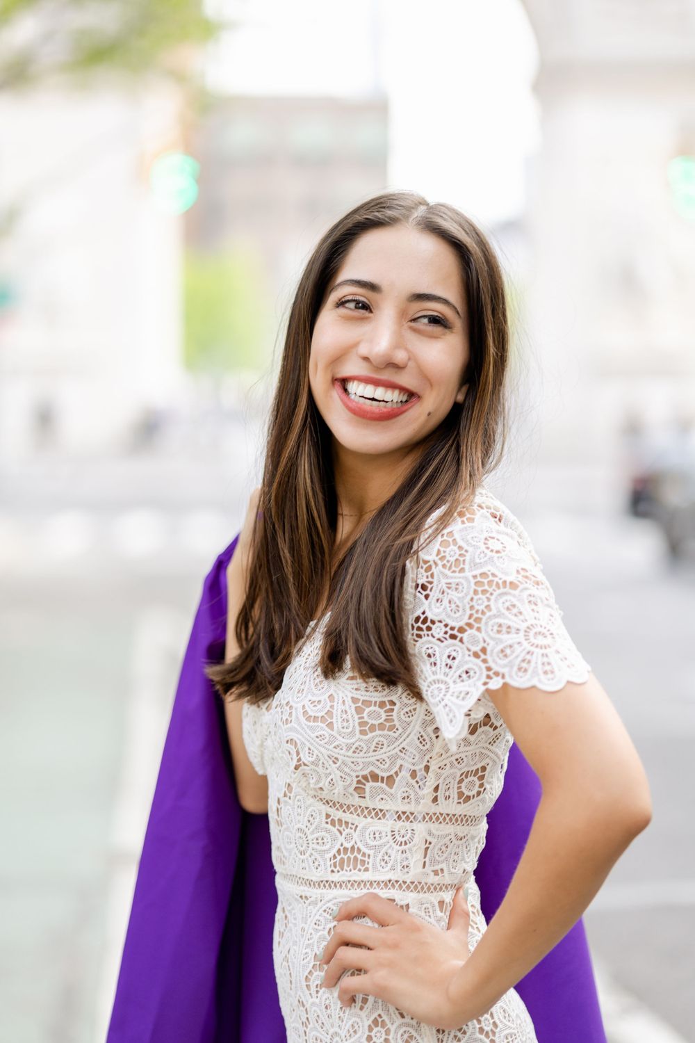 Graduate in white lace dress and purple gown smiles during photo session.