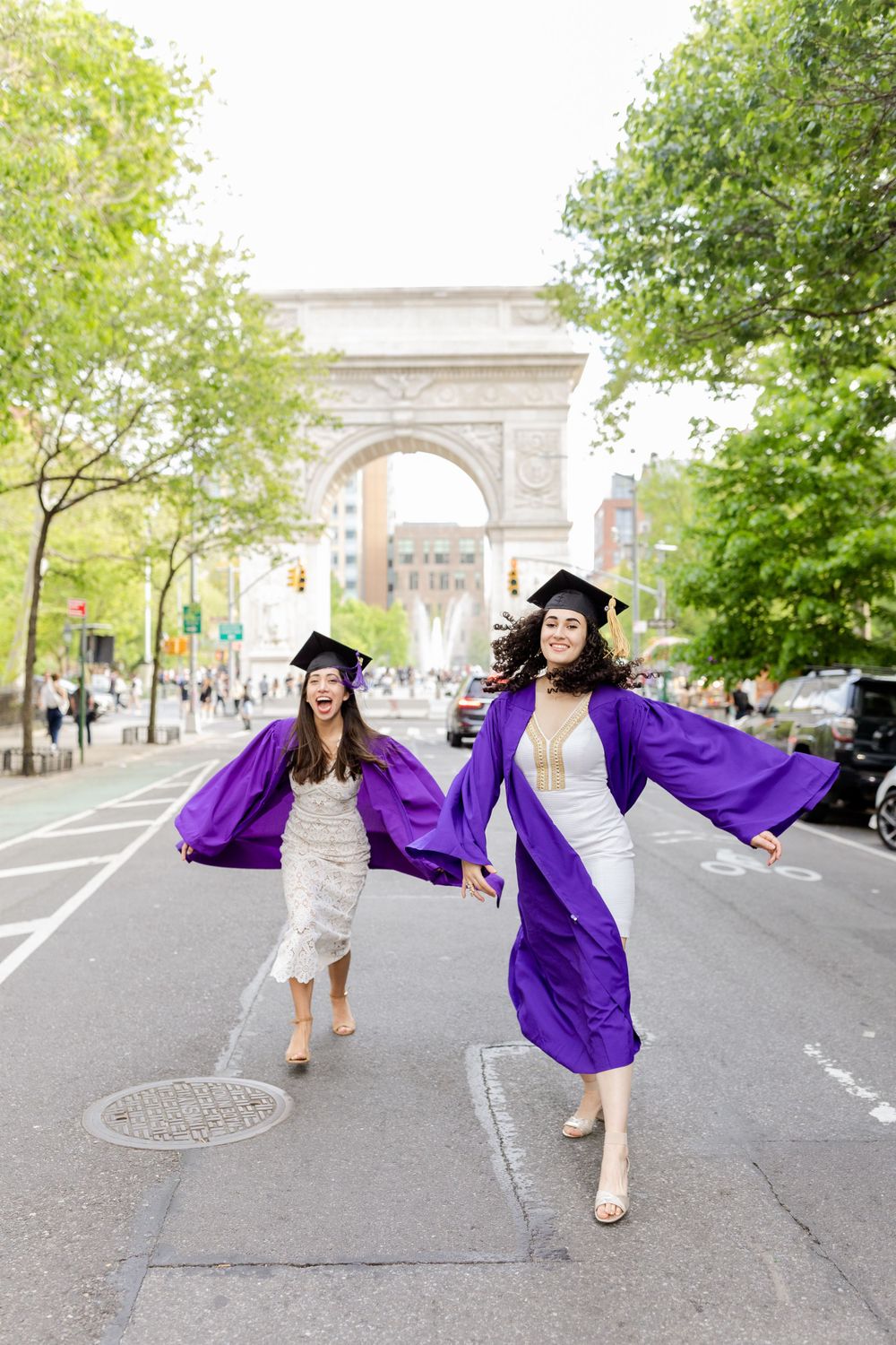 Graduates in purple commencement robes leap joyfully in front of NYC landmark arch.