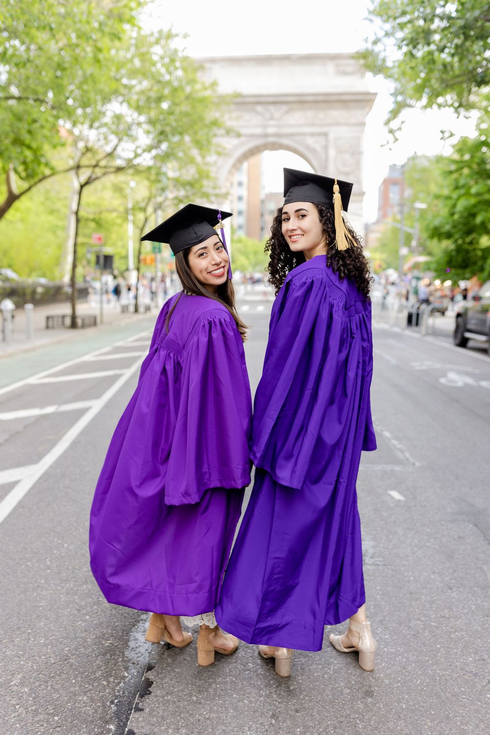 Two graduates in purple graduation gowns pose together in front of Washington Square Arch.