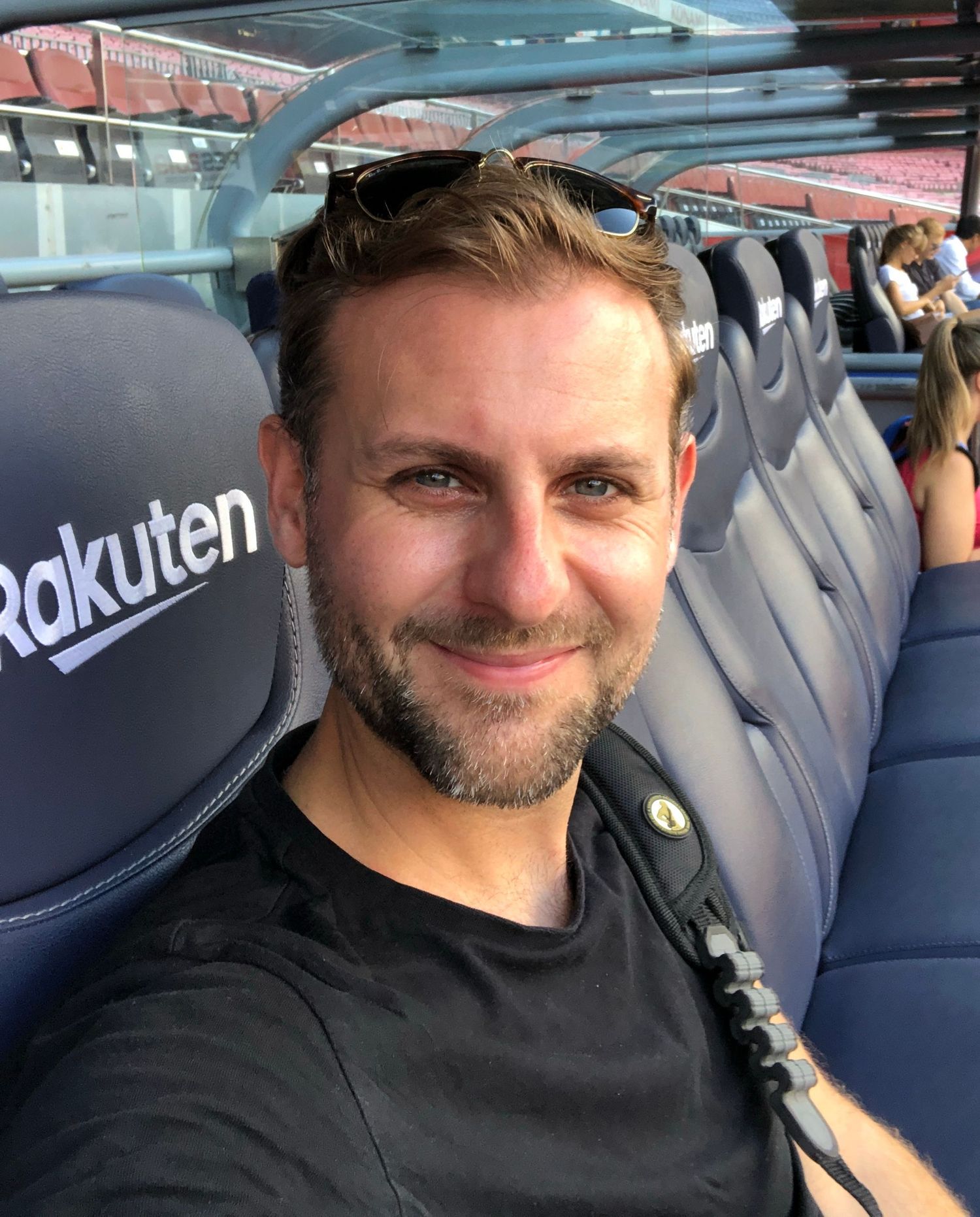 Lee Charlton sitting in stadium seats with Rakuten logo visible in background at sports venue.