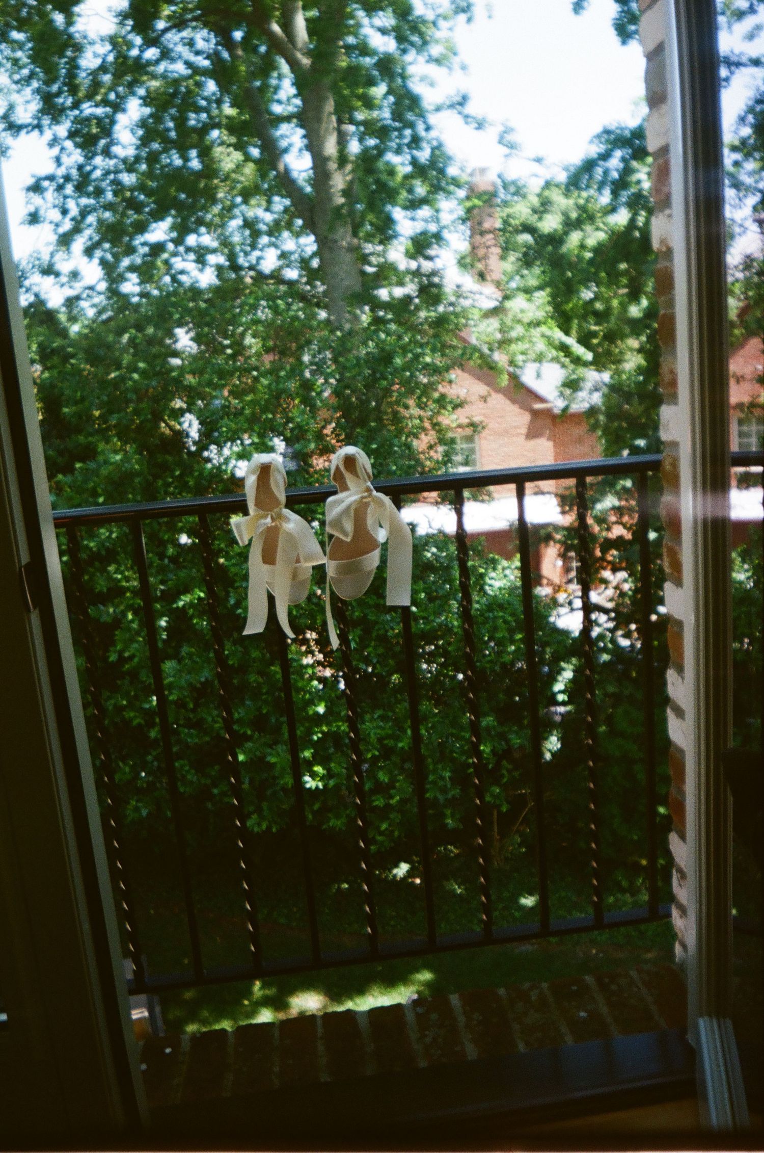 Two stuffed plush toys hanging on a balcony railing with green trees and a brick house in the background.