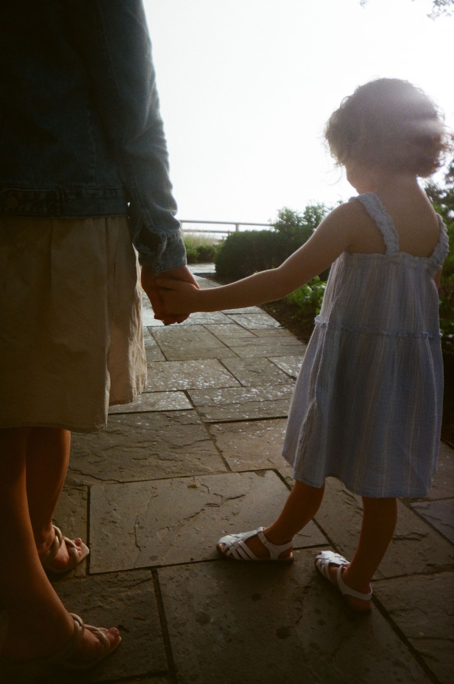 A series of blurred images show a small child learning to walk on a paved surface while holding an adult's hand.