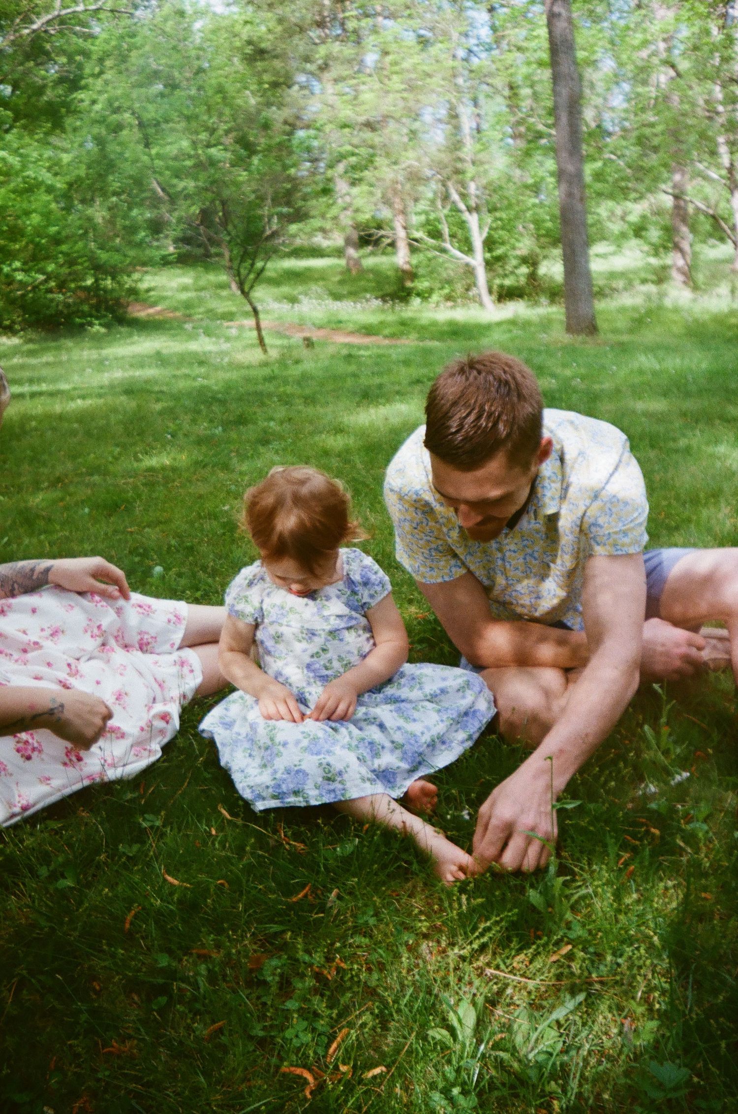 A sweet outdoor moment on a blanket in a lush green garden where two people sit together on a summer day.