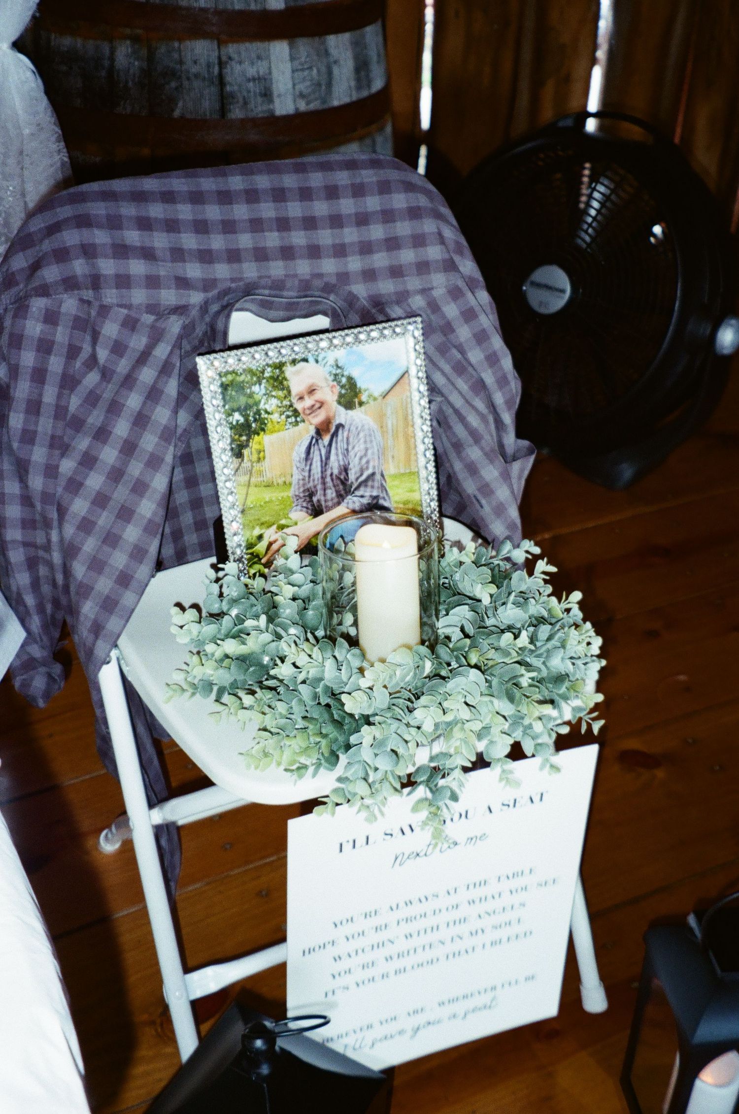 A folding white wooden chair decorated with greenery, a candle, and framed photos for a memorial or celebration display.