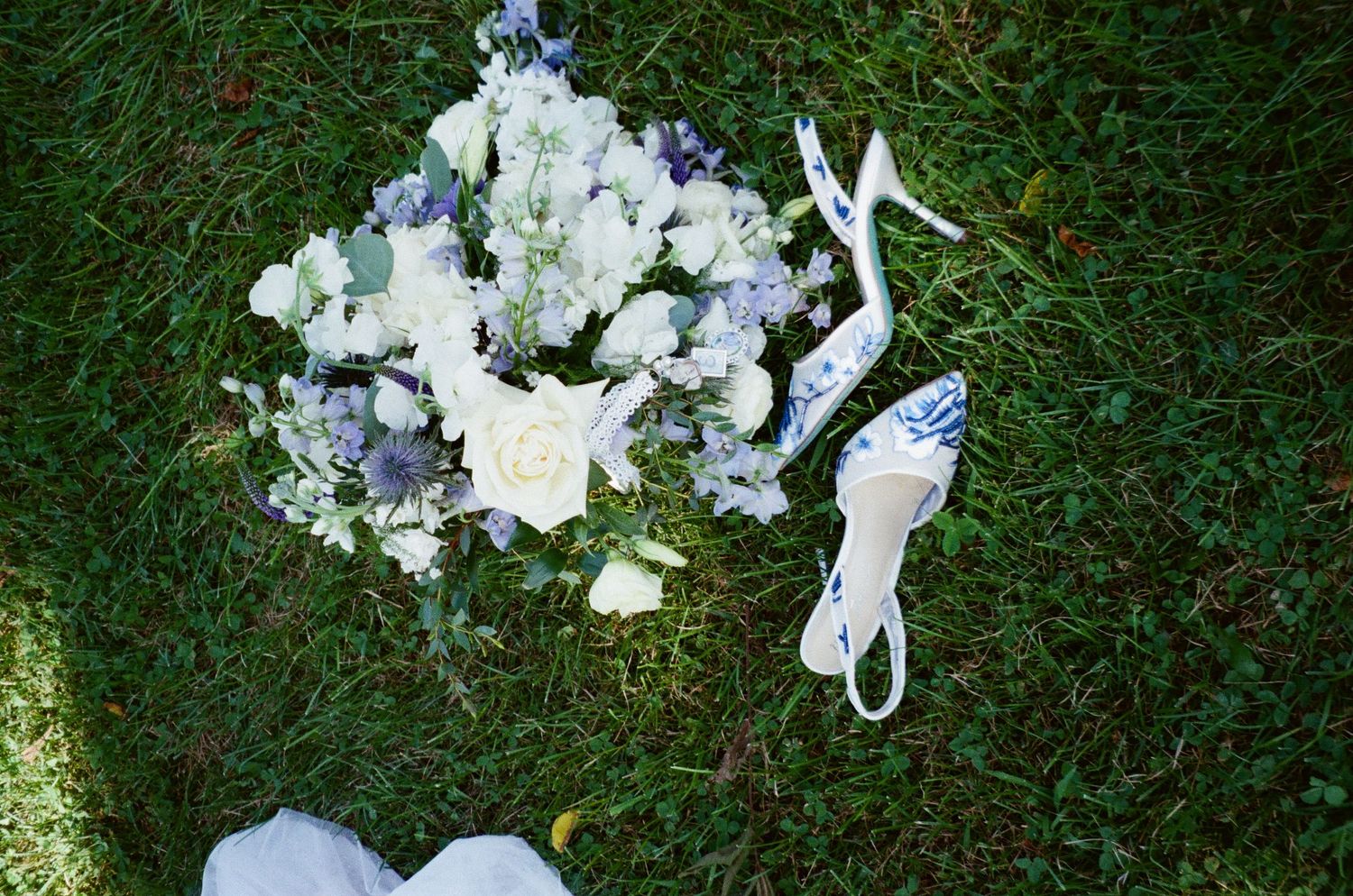 White floral bouquet and elegant bridal heels arranged on green grass in natural lighting.