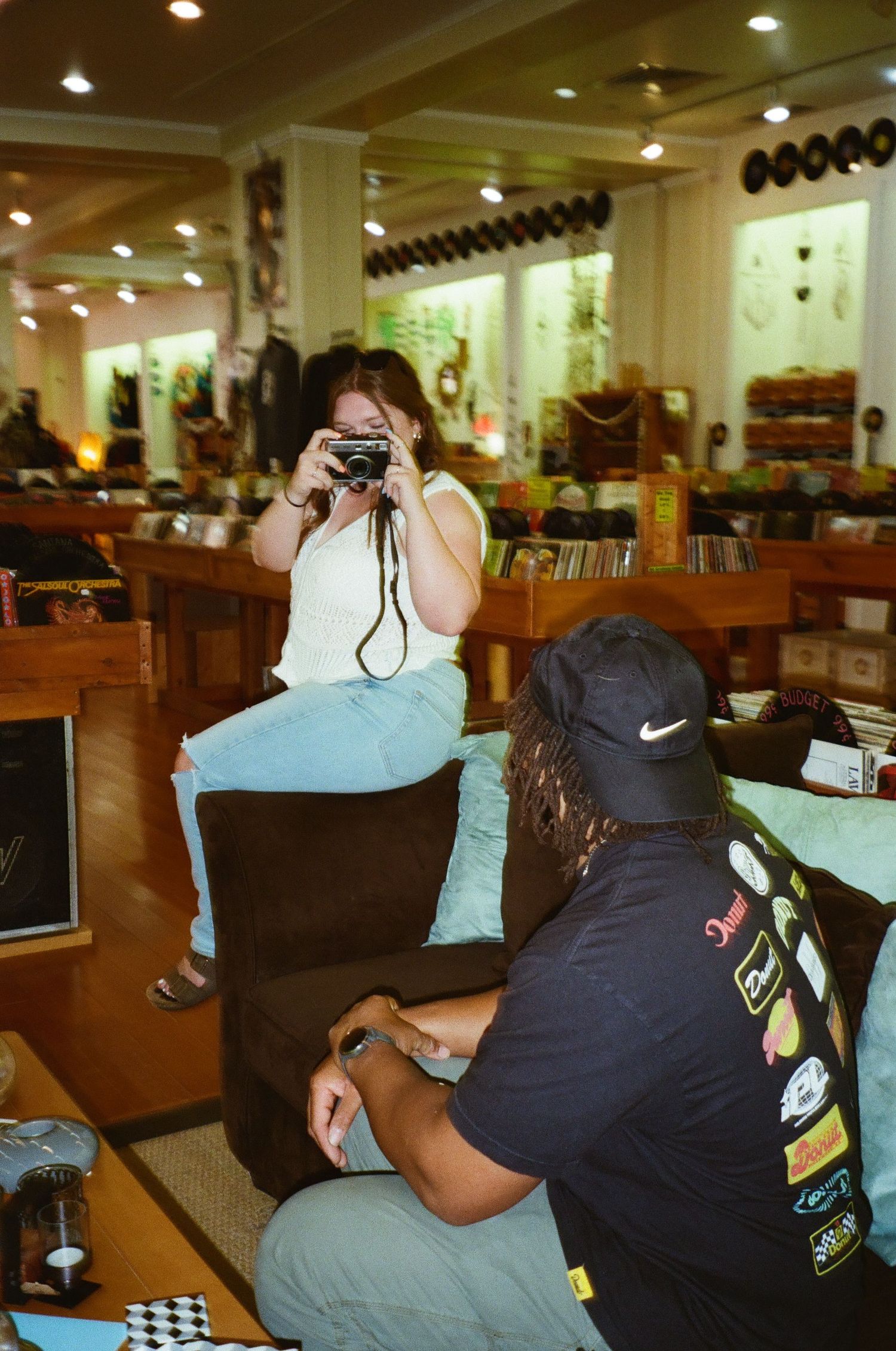Someone takes a photo with a vintage camera in what appears to be a record store or music shop with wooden shelving displays.