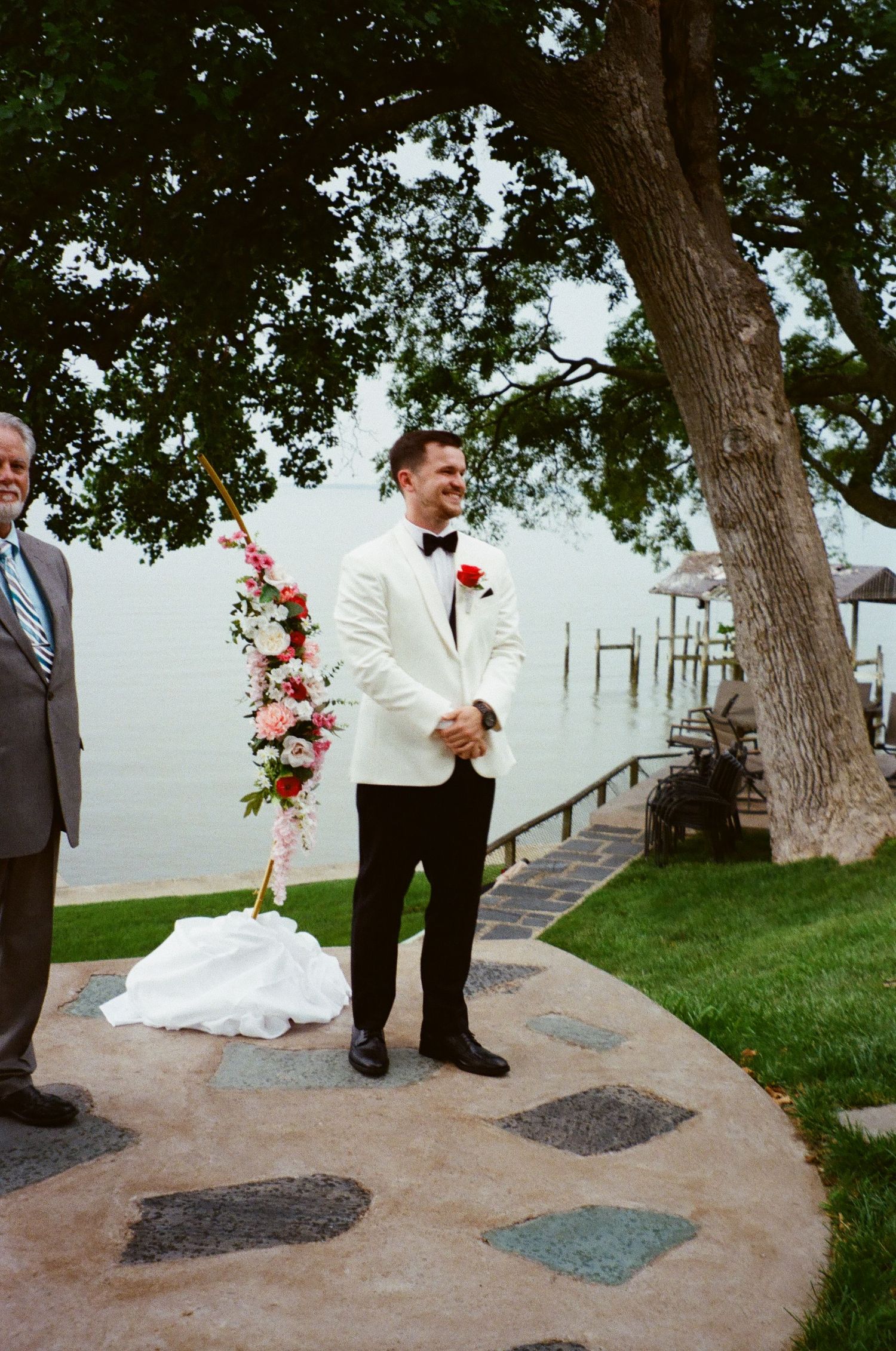 A series of candid wedding photos showing a couple and wedding party members on a stone patio under shady trees by the water.