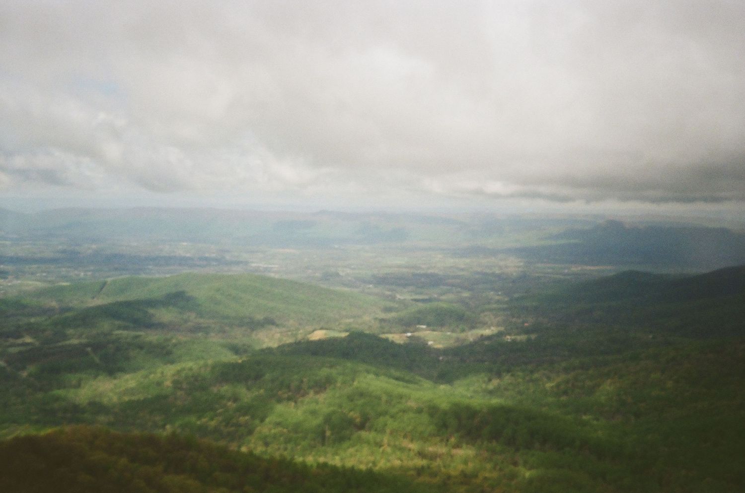 Aerial panoramic view of rolling green hills and misty valleys in a mountainous rural landscape.
