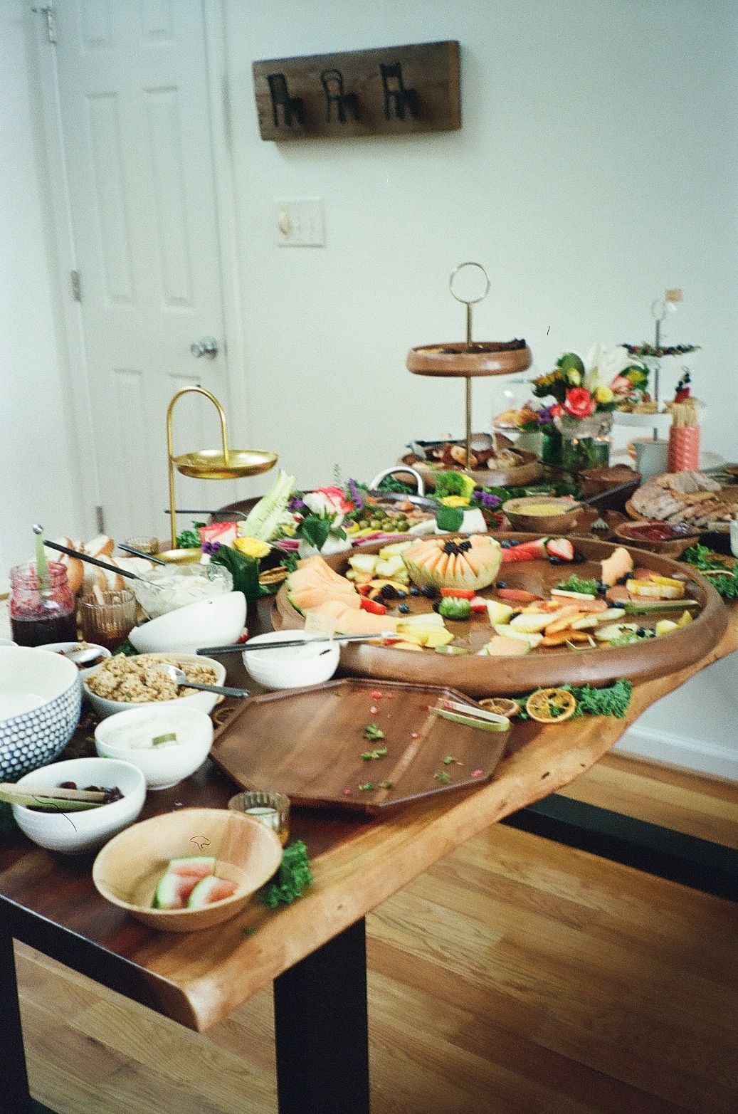 A rustic wooden table set with an elegant grazing board spread featuring charcuterie, cheese, fruits and decorative florals.