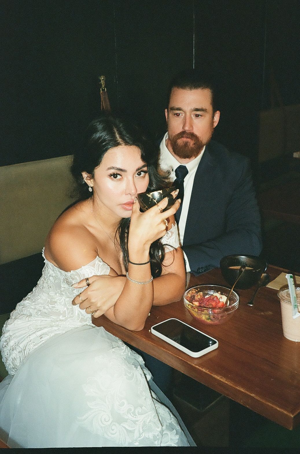 A candid moment at a wedding reception showing a couple seated at a table with a white dress and formal attire.