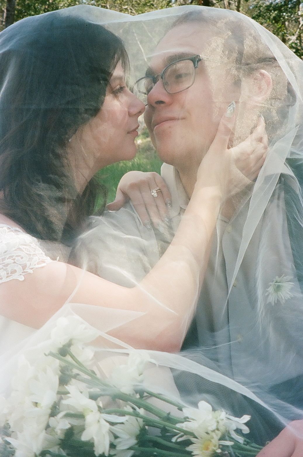 A romantic moment under a delicate white veil with soft natural lighting and floral accents.