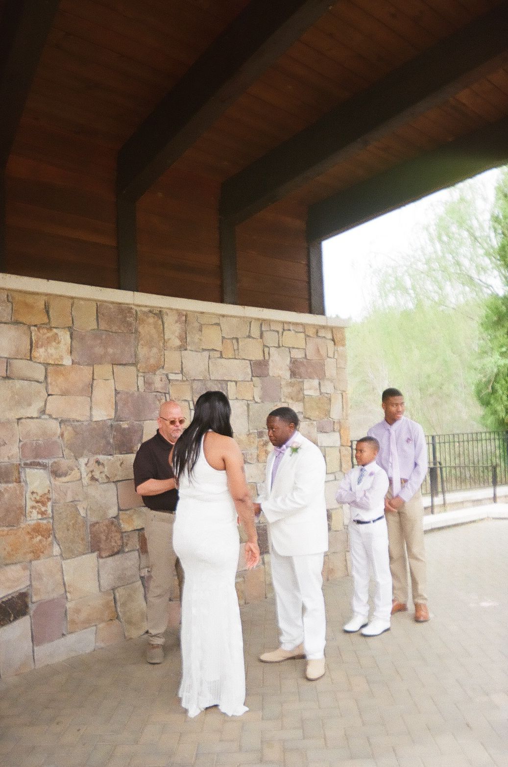 Small wedding ceremony taking place under a covered stone patio with wooden beams.
