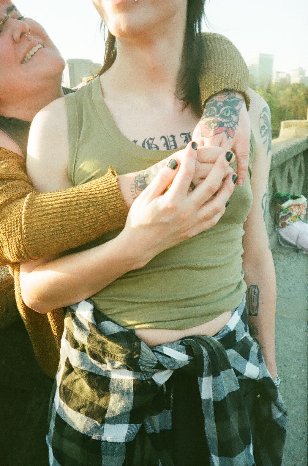 Close up photo showing colorful tattoos and plaid shirt tied at waist in warm sunlit outdoor setting.