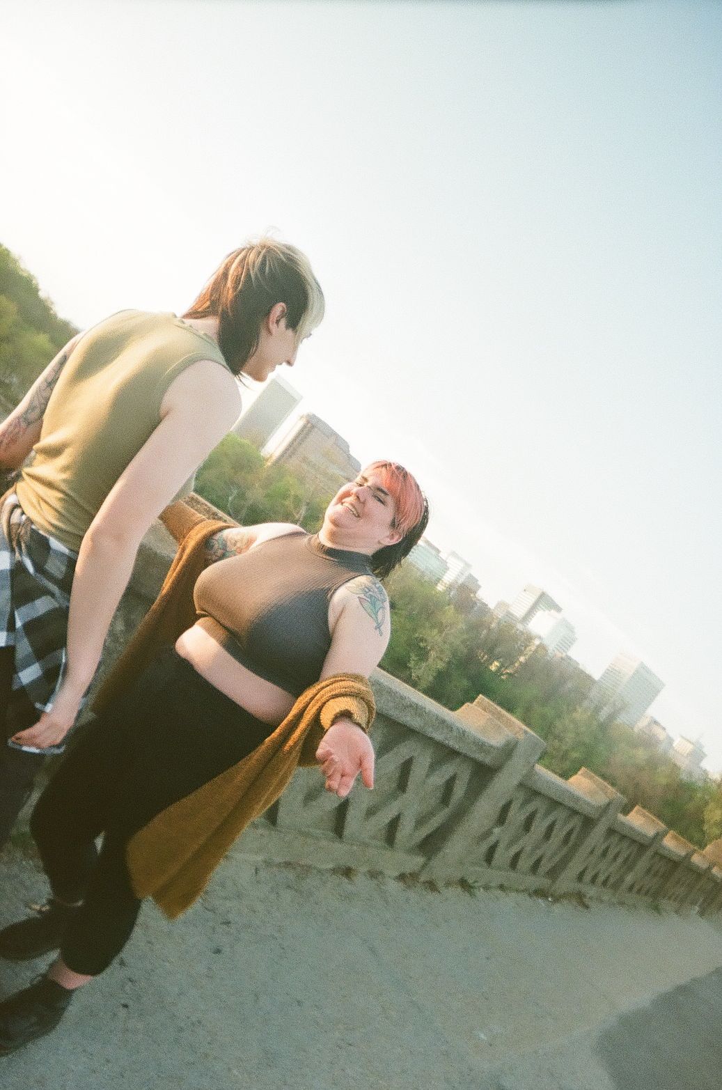 Two people in casual clothing lean against a stone wall while enjoying a sunny outdoor moment.
