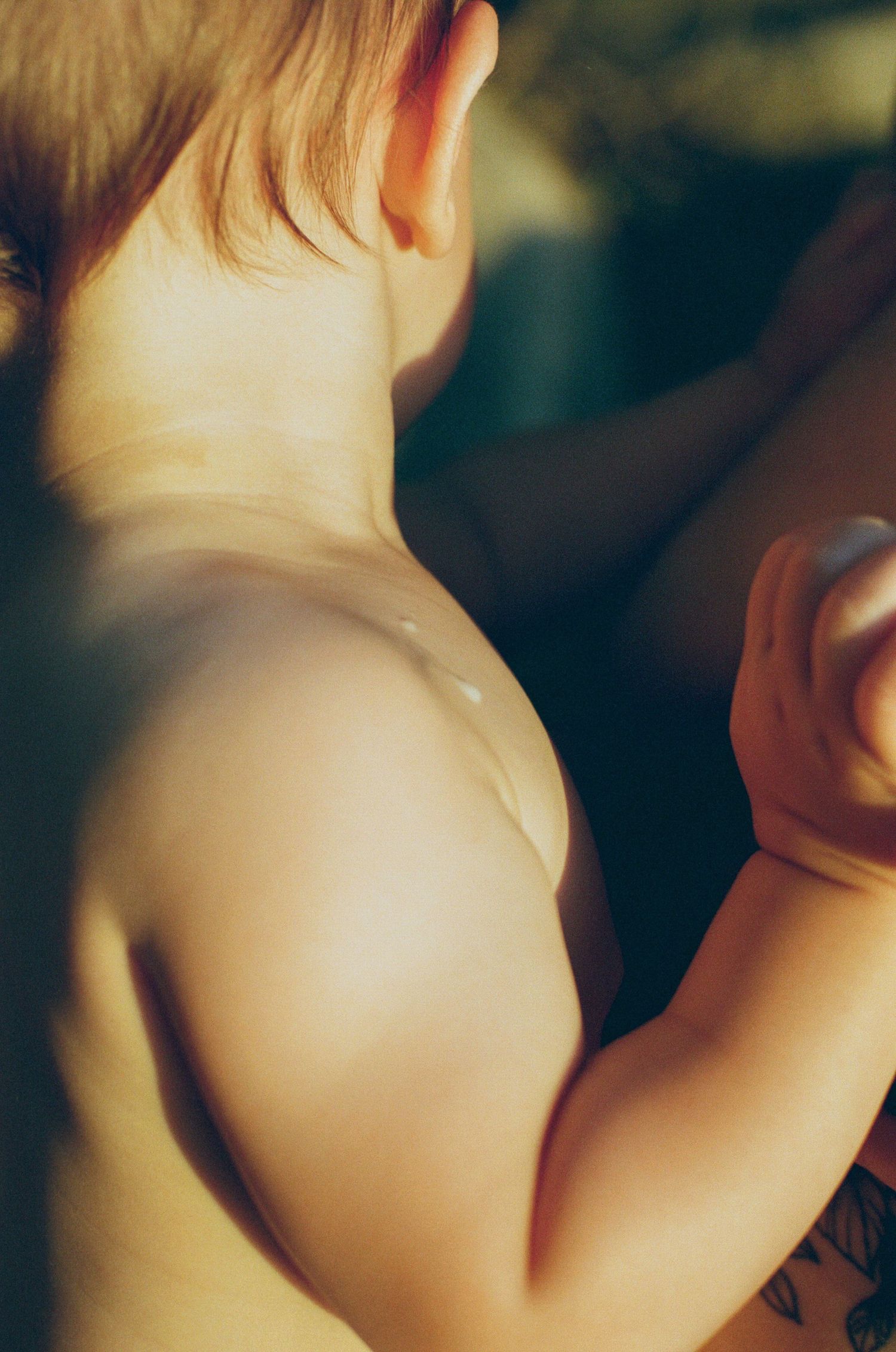 Close-up of a young baby's bare back and shoulder bathed in warm golden sunlight.