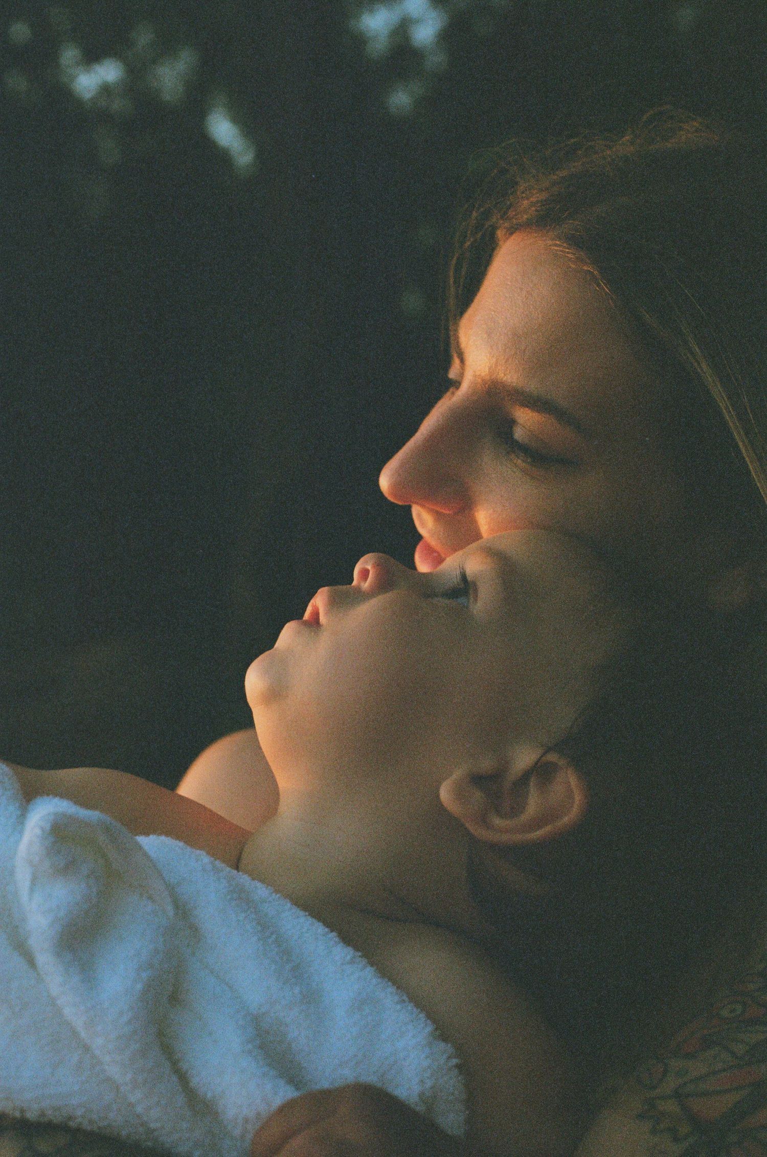 A mother tenderly holds her newborn baby in warm golden light outdoors, captured in a intimate film photography portrait.