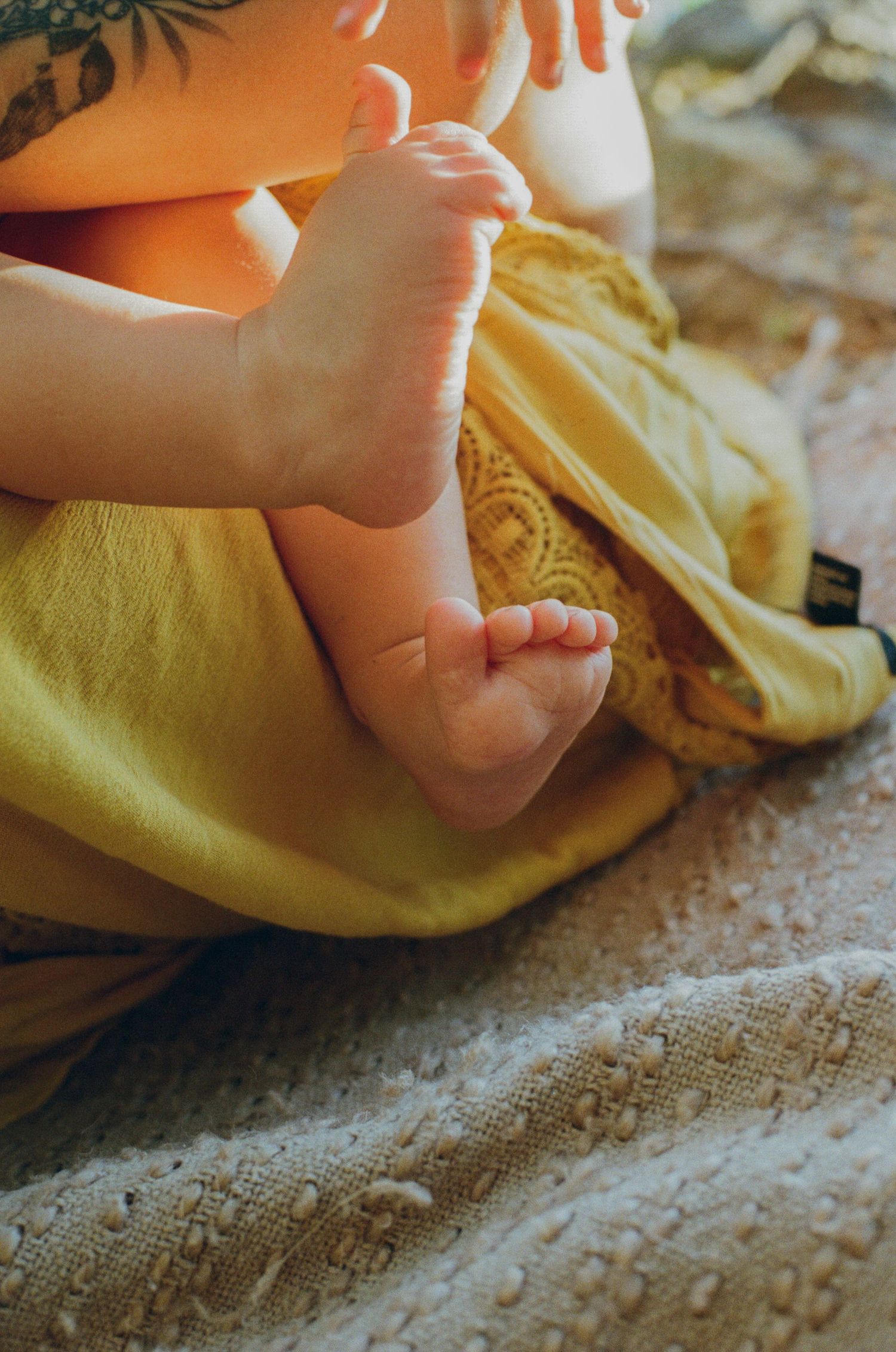 Close-up of tiny baby feet resting on yellow fabric blankets on a textured carpet.