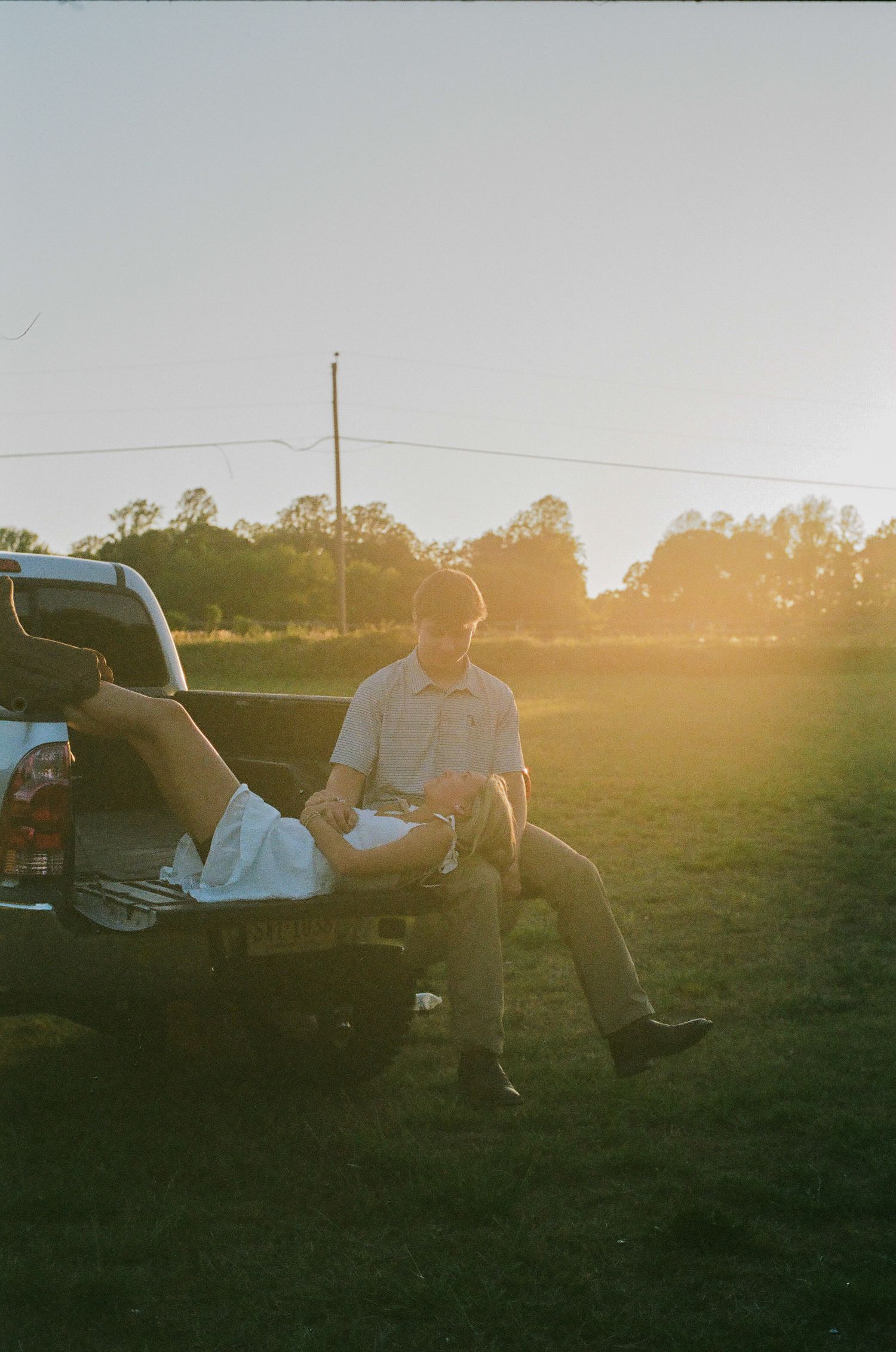 Two people sitting on the tailgate of a pickup truck in a field during golden hour sunset.