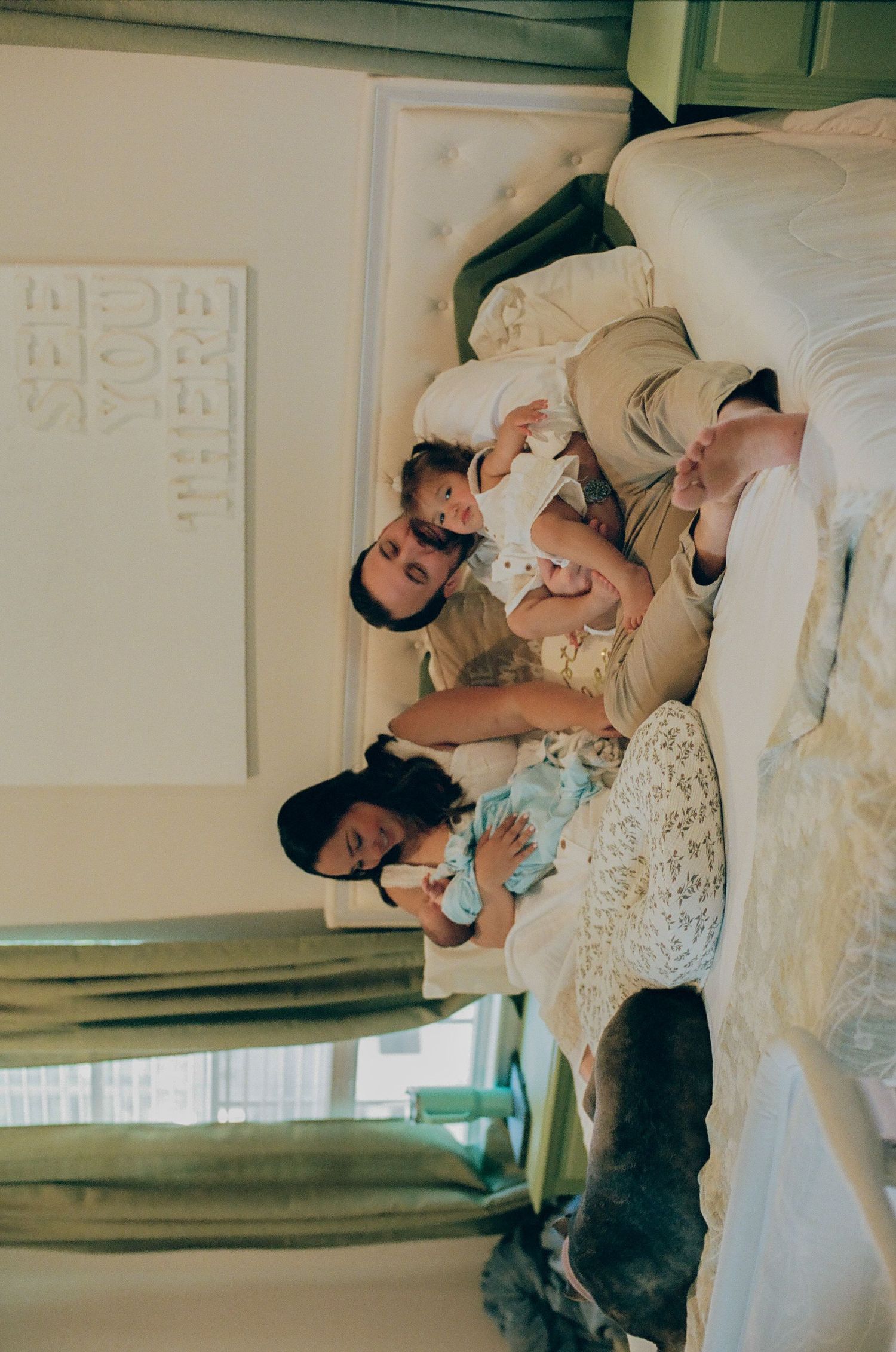 Family portrait with parents holding two young children in a bright, decorated room.