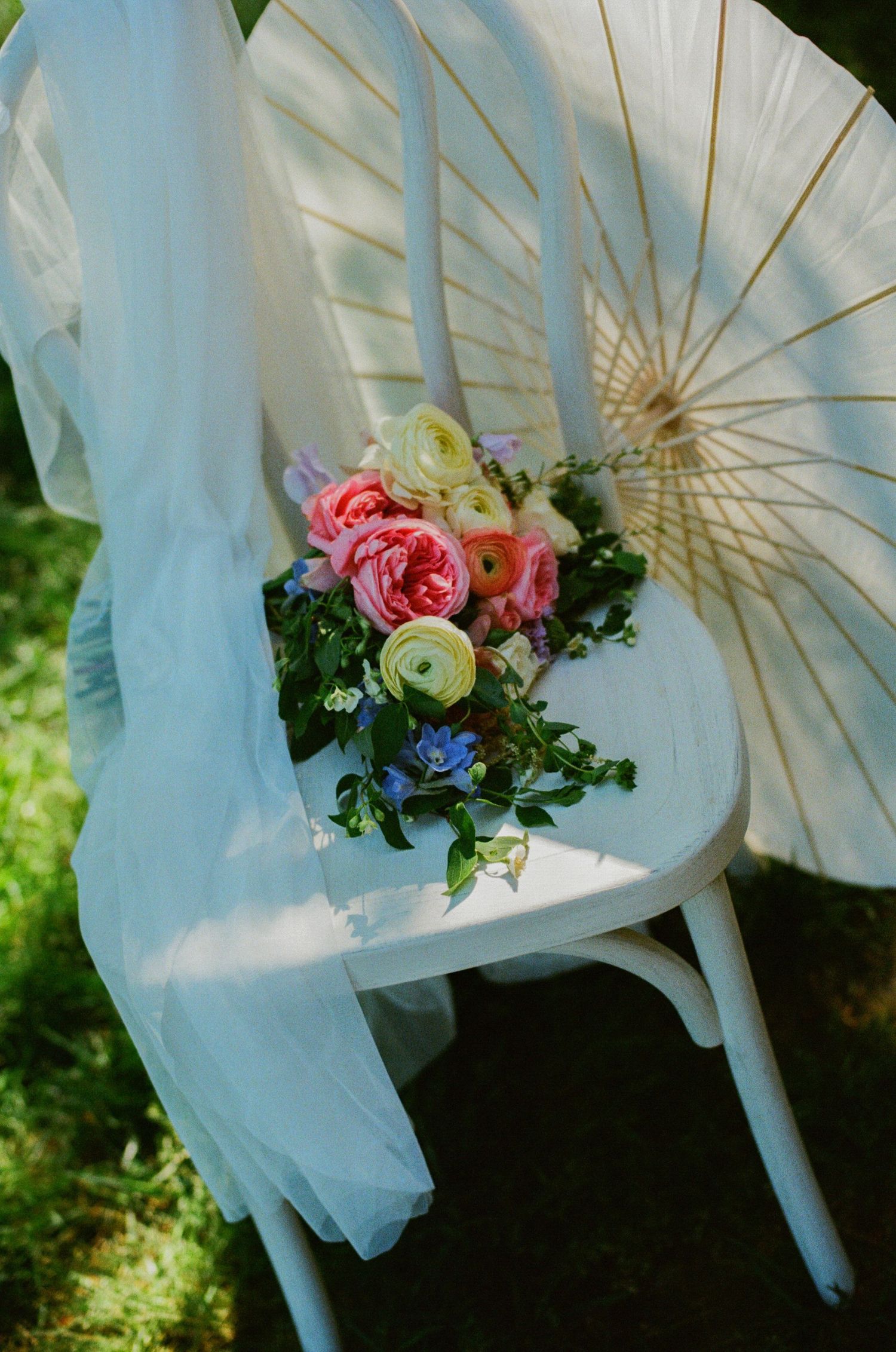 Colorful spring bouquet with pink roses and blue flowers on a white chair with a parasol outdoors.