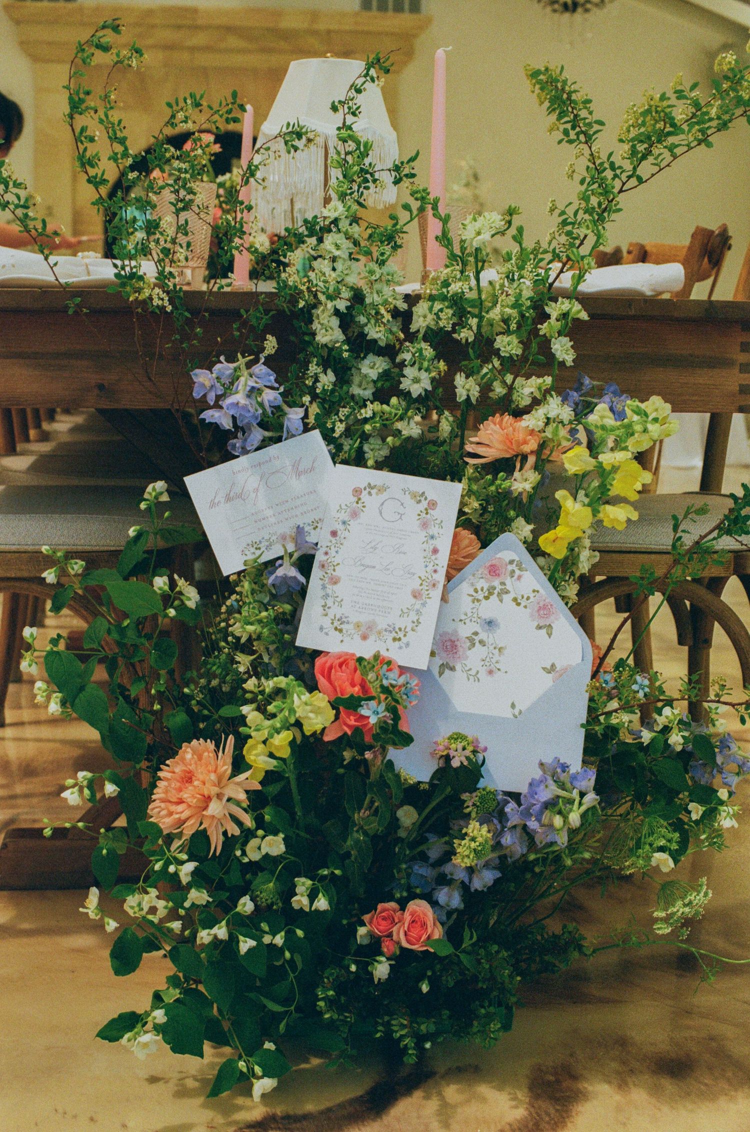 Lush floral arrangement with colorful blooms and wedding stationery cards displayed on a rustic wooden table.