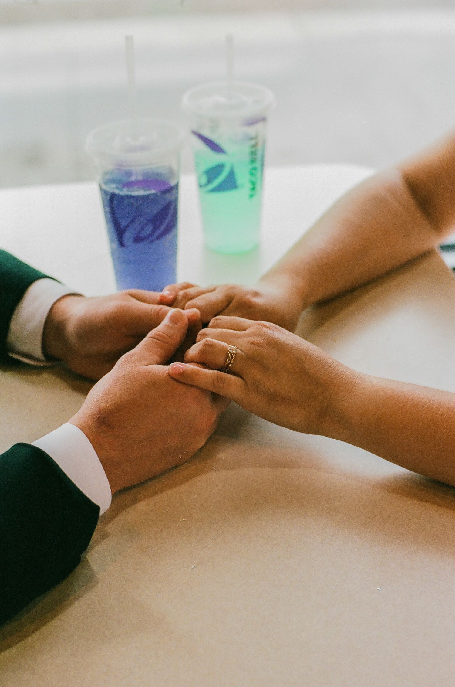 Couple holding hands at Taco Bell table with colorful drinks, woman wearing gold engagement ring, romantic fast food wedding.