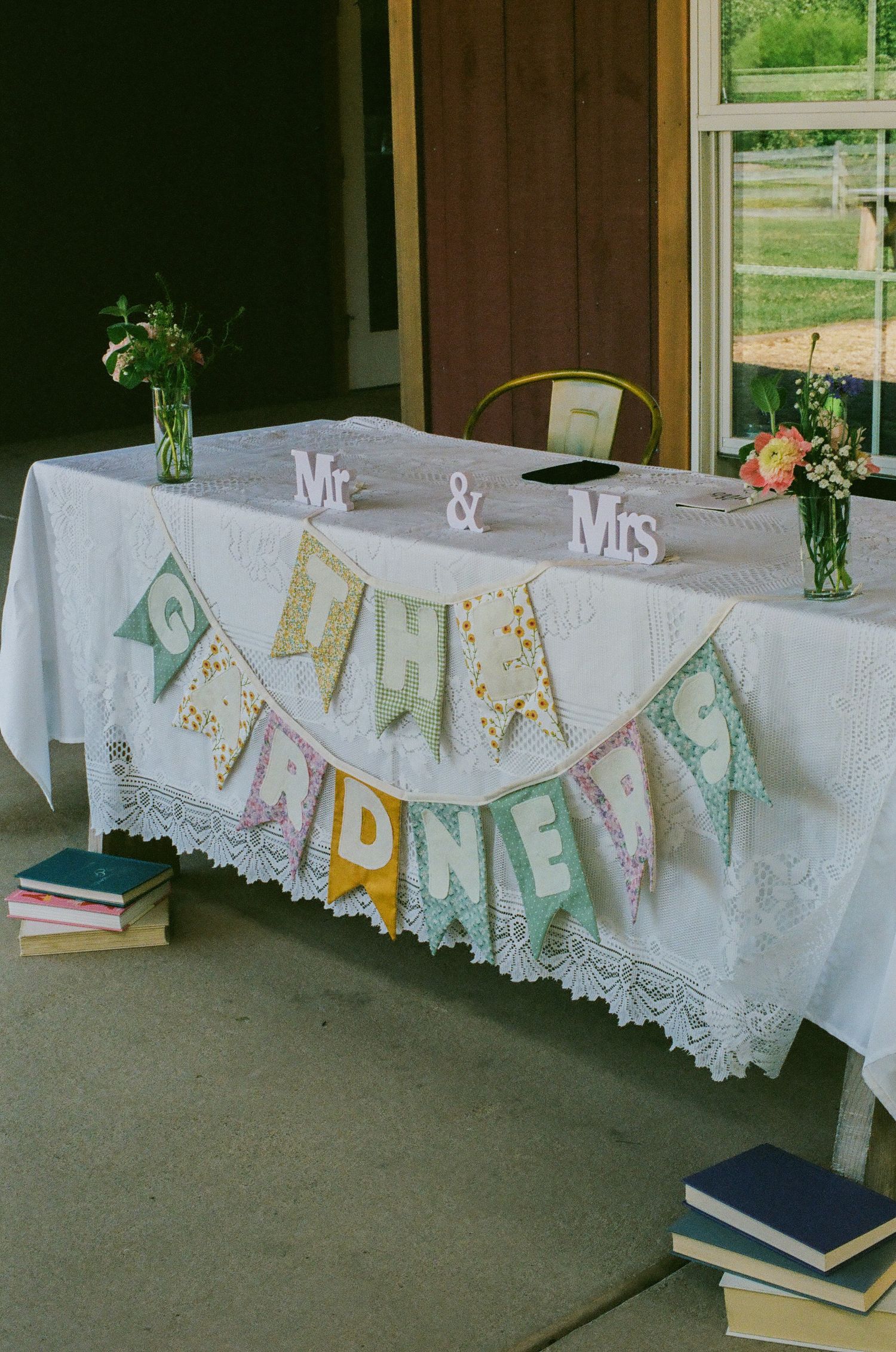 Wedding reception table with Mr. & Mrs. banner, floral arrangements, and colorful bunting spelling the couple's name.