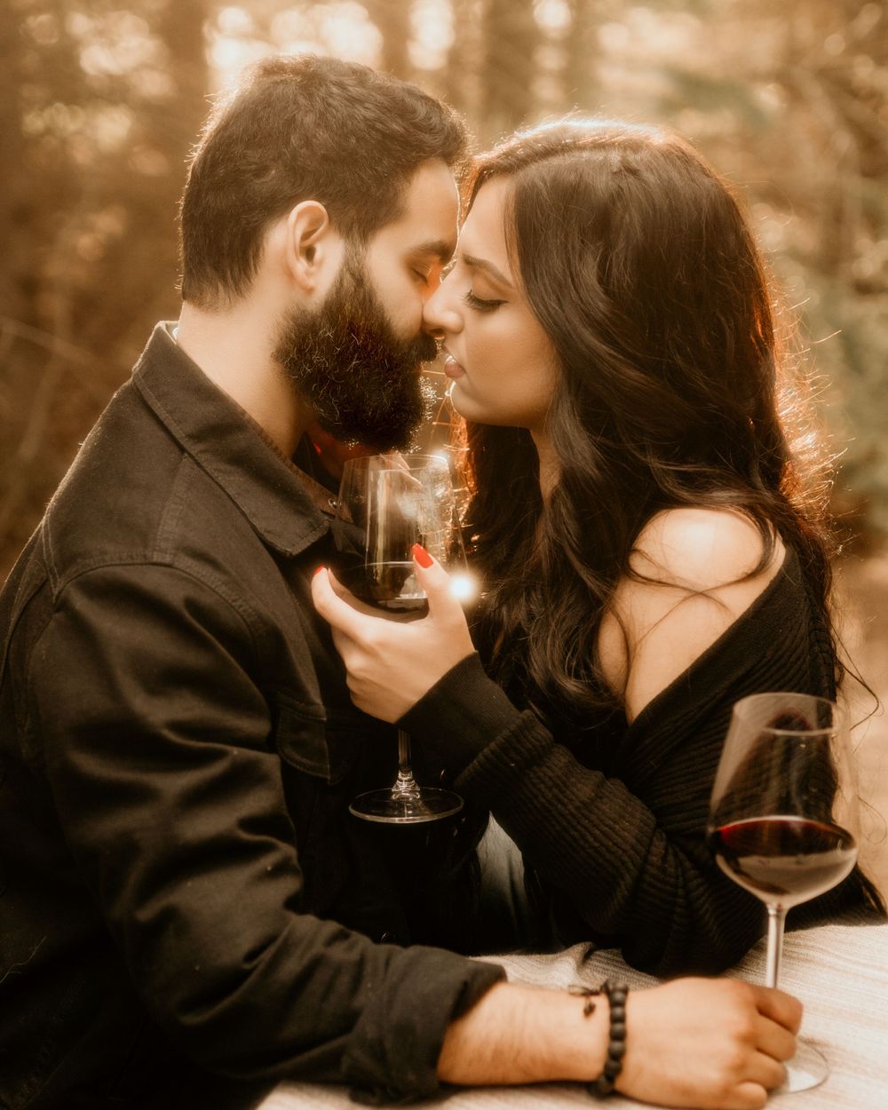 Romantic couple sharing an intimate moment with wine glasses at sunset in a warm sepia-toned setting.