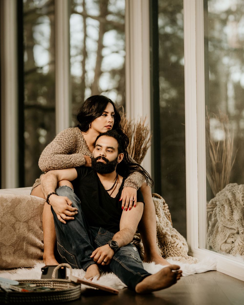A cozy couple lounges together by large windows in a rustic cabin setting during golden hour.