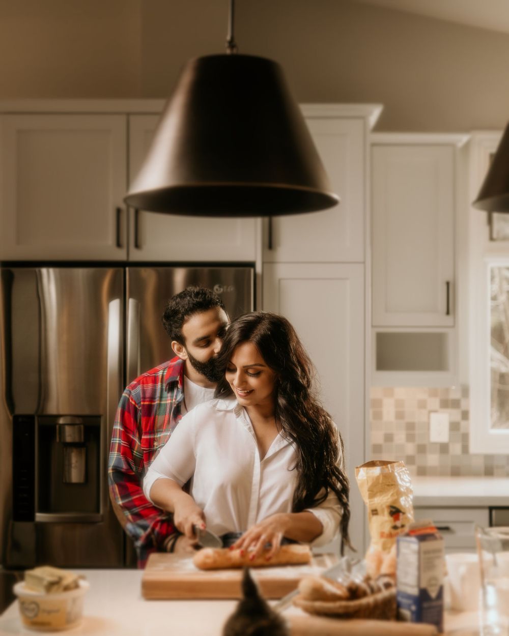 A couple shares an intimate moment while preparing food together in a modern kitchen with white cabinets.