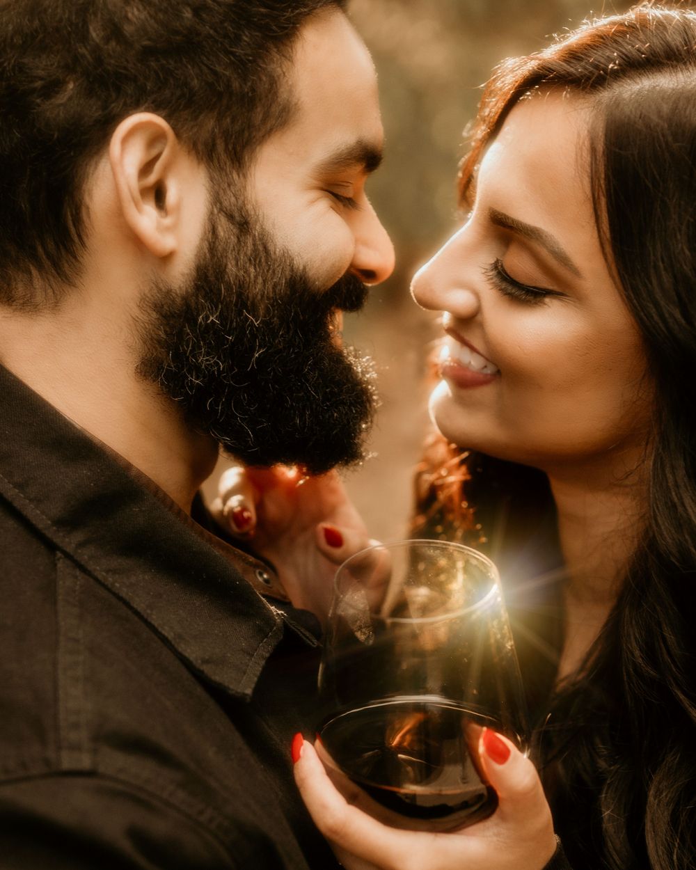 A couple gazes lovingly at each other while sharing wine in warm golden lighting.