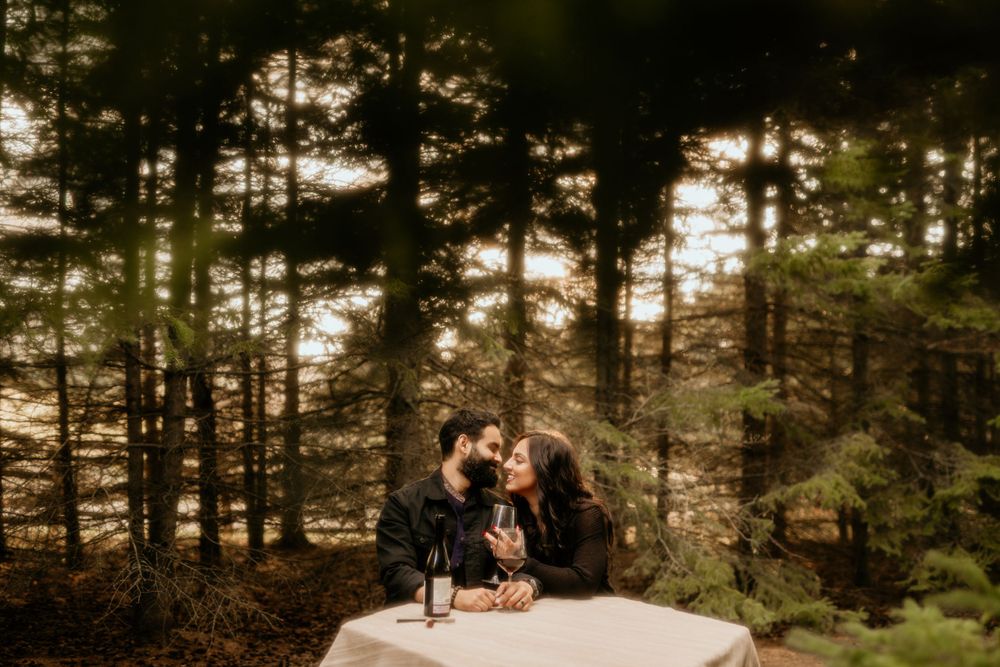 Couple sharing intimate moment while sitting on rock formation in misty forest setting.