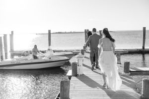 Newlyweds walking hand in hand on a wooden pier with boats in the background.