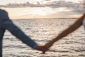 Silhouetted hands forming a heart shape against a sunset ocean view.