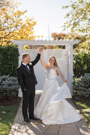 Joyful wedding couple celebrating under a white garden arbor surrounded by autumn foliage.