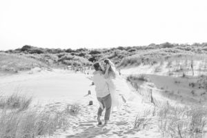 Person in white dress running joyfully through sand dunes on sunny day.