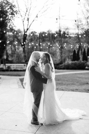 A romantic black and white wedding photo capturing a tender moment between newlyweds dancing outdoors with twinkling lights.