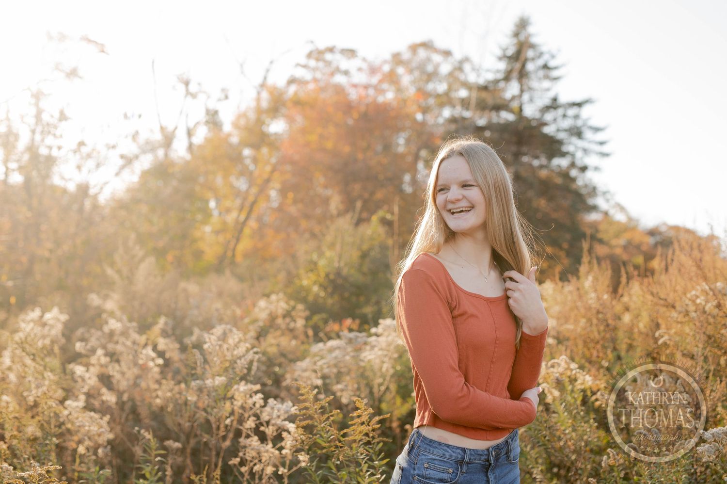 A portrait in golden autumn light with a rust-colored sweater and casual style among tall grasses.