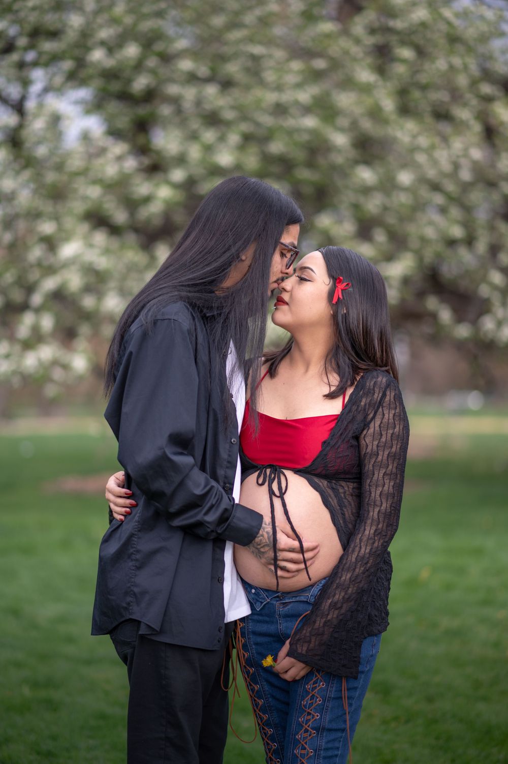 A tender romantic moment between two people in a park setting with springtime blossoms in the background.