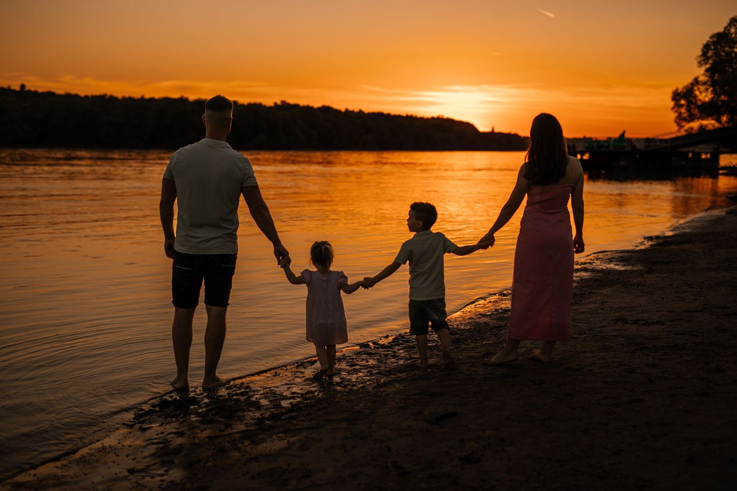 Silhouettes of a family holding hands while walking along beach shore during golden sunset.