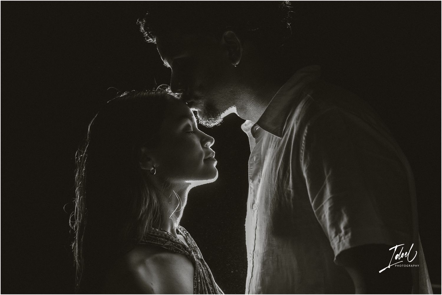 Artistic black and white silhouette portrait of two people in intimate moment, shot with dramatic lighting and shadow.